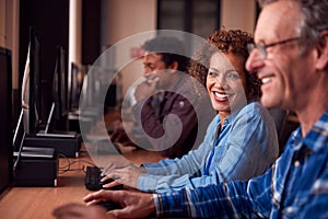 Group Of Mature Adult Students In Class Working At Computers In College Library