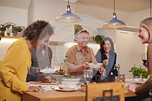 Group Of Mature Friends Meeting At Home Serving Food At Dinner Party And Drinking Wine Together