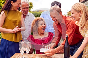 Group Of Mature Friends At Surprise Birthday Party For Woman In Garden With Cake And Champagne