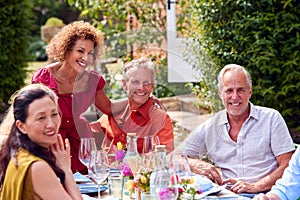 Group Of Mature Friends Talking Around Table At Summer Dinner Party In Garden At Home