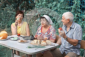 A group of mature people dine with natural products at a table in the garden