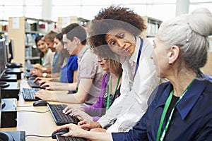 Group Of Mature Students Working At Computers With Tutor