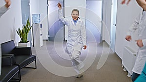 Group of mature and young doctors and nurses in a modern hospital corridor dancing in front of the camera and feeling