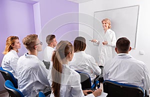 Group of medical students attentively listening to lecture of female teacher in classroom