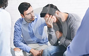 Group members comforting crying addicted man at rehab session