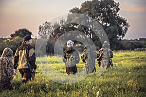 Group of men hunters going through tall grass on rural field at sunset during hunting season