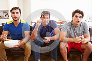 Group Of Men Sitting On Sofa Watching Sport Together