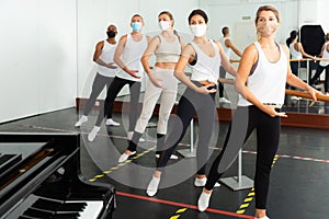 Group of men and women in protective masks practicing at ballet barre