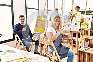 Group of middle age artist at art studio pointing with hand finger to the side showing advertisement, serious and calm face