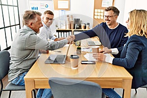 Group of middle age business workers smiling and looking partners handshake at the office