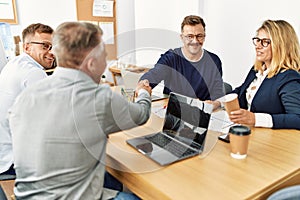 Group of middle age business workers smiling and looking partners handshake at the office