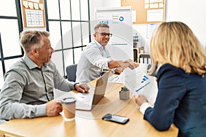 Group of middle age business workers smiling and looking partners handshake at the office