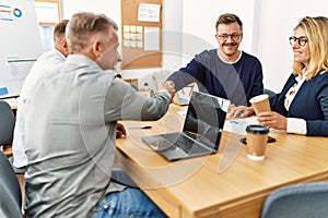 Group of middle age business workers smiling and looking partners handshake at the office