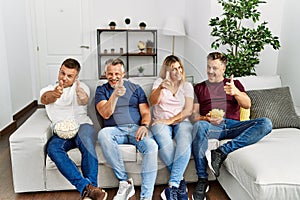 Group of middle age people sitting on the sofa at home pointing fingers to camera with happy and funny face