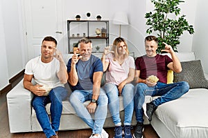 Group of middle age people sitting on the sofa at home smiling and confident gesturing with hand doing small size sign with