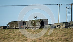 Group of military trucks traversing a dusty dirt road the cargo bed of the vehicle covered in a tarp