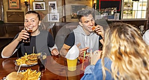 Group of millennials friends eating at fast food indoors in irish pub restaurant. Happy people partying and eating together. Young