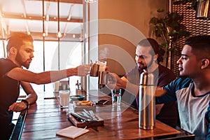 Group of mixed race young men clink glasses in lounge bar. Multiracial friends having fun in cafe