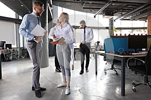 Group of modern business people are talking and smiling while standing in the office hallway