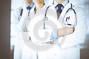 Group of modern doctors standing as a team with crossed arms and stethoscopes in hospital office. Physicians ready to