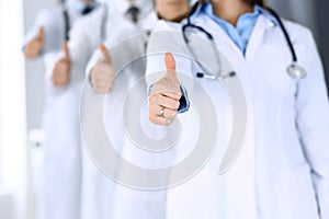 Group of modern doctors standing as a team with thumbs up in hospital office. Physicians ready to examine and help