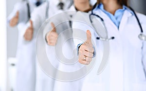 Group of modern doctors standing as a team with thumbs up in hospital office. Physicians ready to examine and help