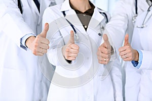 Group of modern doctors standing as a team with thumbs up in hospital office. Physicians ready to examine and help