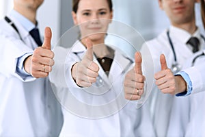 Group of modern doctors standing as a team with thumbs up in hospital office. Physicians ready to examine and help