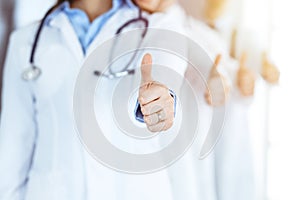 Group of modern doctors standing as a team with thumbs up in sunny hospital. Medical help, insurance in health care