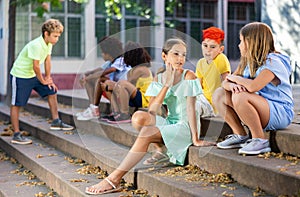Positive tweenagers friendly blabbing while sitting on steps outdoors photo