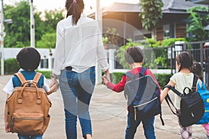 Group of mother and kids holding hands going to school with schoolbag. Mom bring children walk to school by bus together with