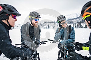 Group of mountain bikers standing on road outdoors in winter, talking.
