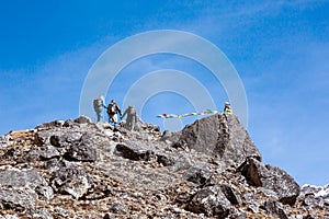 Group of Mountain Climbers approaching to rocky Summit with buddhist Flags