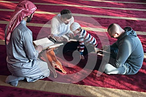 Group of muliethnic religious muslim young people praying and reading Koran together inside beautiful modern mosque
