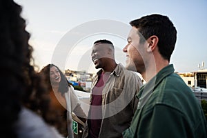 Group of multi-cultural friends laughing and socializing on rooftop terrace at dusk.