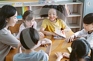 Group of Multi-ethnic happy elementary school and Female Asian teacher sitting on chairs in circle around with them and talking in