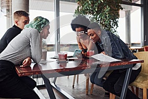 Group of multi ethnic people with alternative girl with green hair is working together by the table indoors