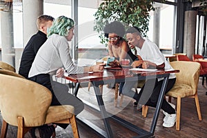 Group of multi ethnic people with alternative girl with green hair is working together by the table indoors