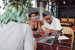 Group of multi ethnic people with alternative girl with green hair is working together by the table indoors