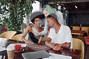 Group of multi ethnic people with alternative girl with green hair is working together by the table indoors