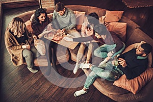 Group of multi ethnic young friends eating pizza in home interior