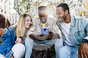 Group of multi-ethnic young friends using mobile phone sitting together outdoor