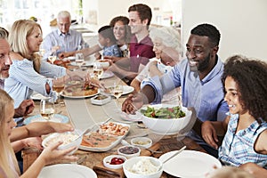 Group Of Multi-Generation Family And Friends Sitting Around Table And Enjoying Meal