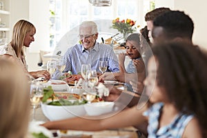 Group Of Multi-Generation Family And Friends Sitting Around Table And Enjoying Meal