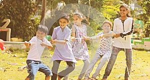 Group of multi racial children playing Tug of war game kindergarten - Multi ethnic kids playing outdoor games againt