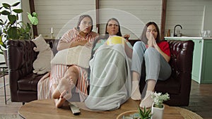 Group of multicultural women watching thriller on digital TV at home