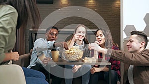 Group of multiethnic happy friends playing block removal game and laughing and rejoicing at a bowl of popcorn having fun together