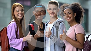 Group of multiethnic students with backpacks showing thumbs-up, education