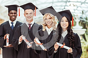 group of multiethnic students with diplomas in graduation hats standing