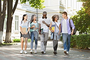 Group of multiethnic students walking together outdoors in college campus photo